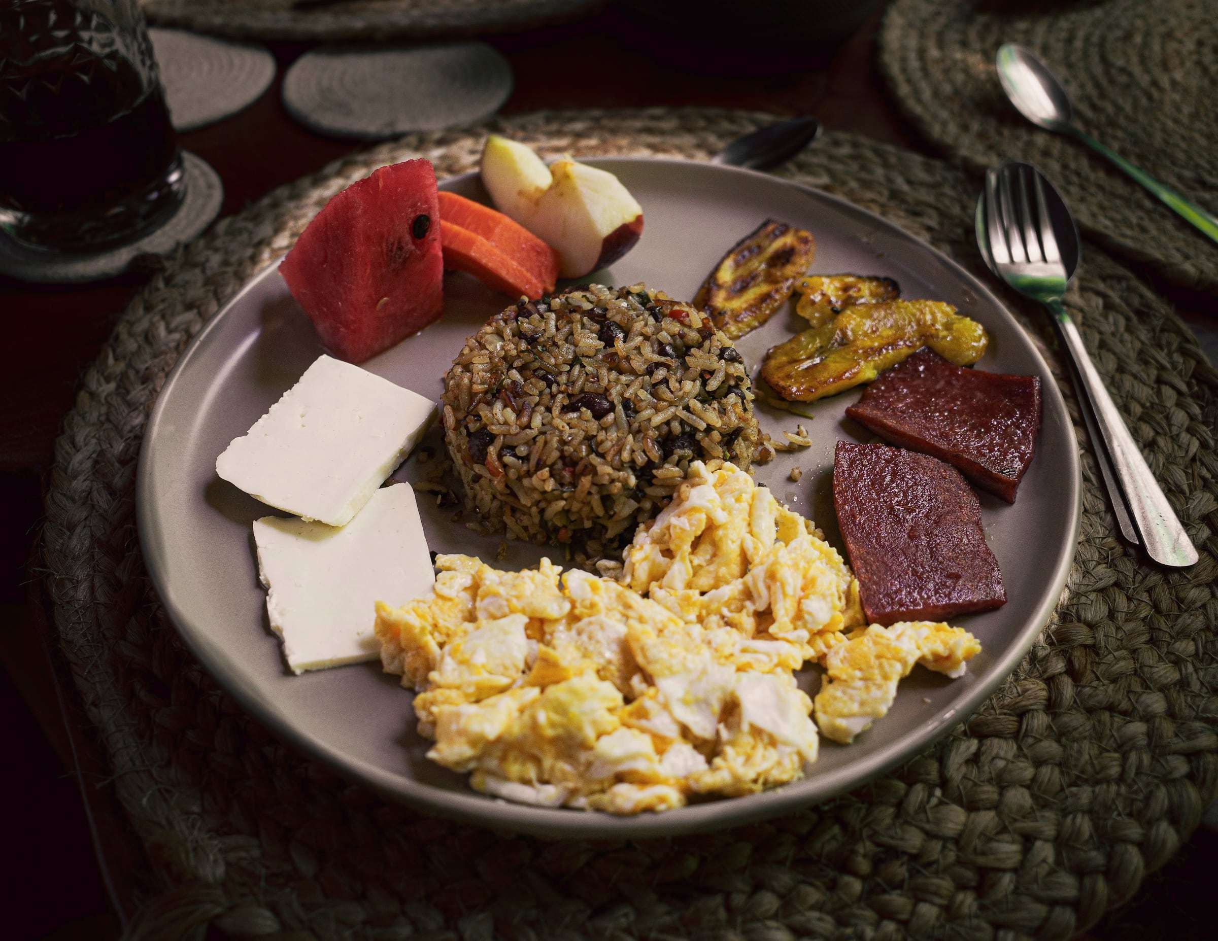 Conga breakfast plate: gallo pinto, scrambled eggs, sweet plantain, fresh cheese and fruit on a woven placemat