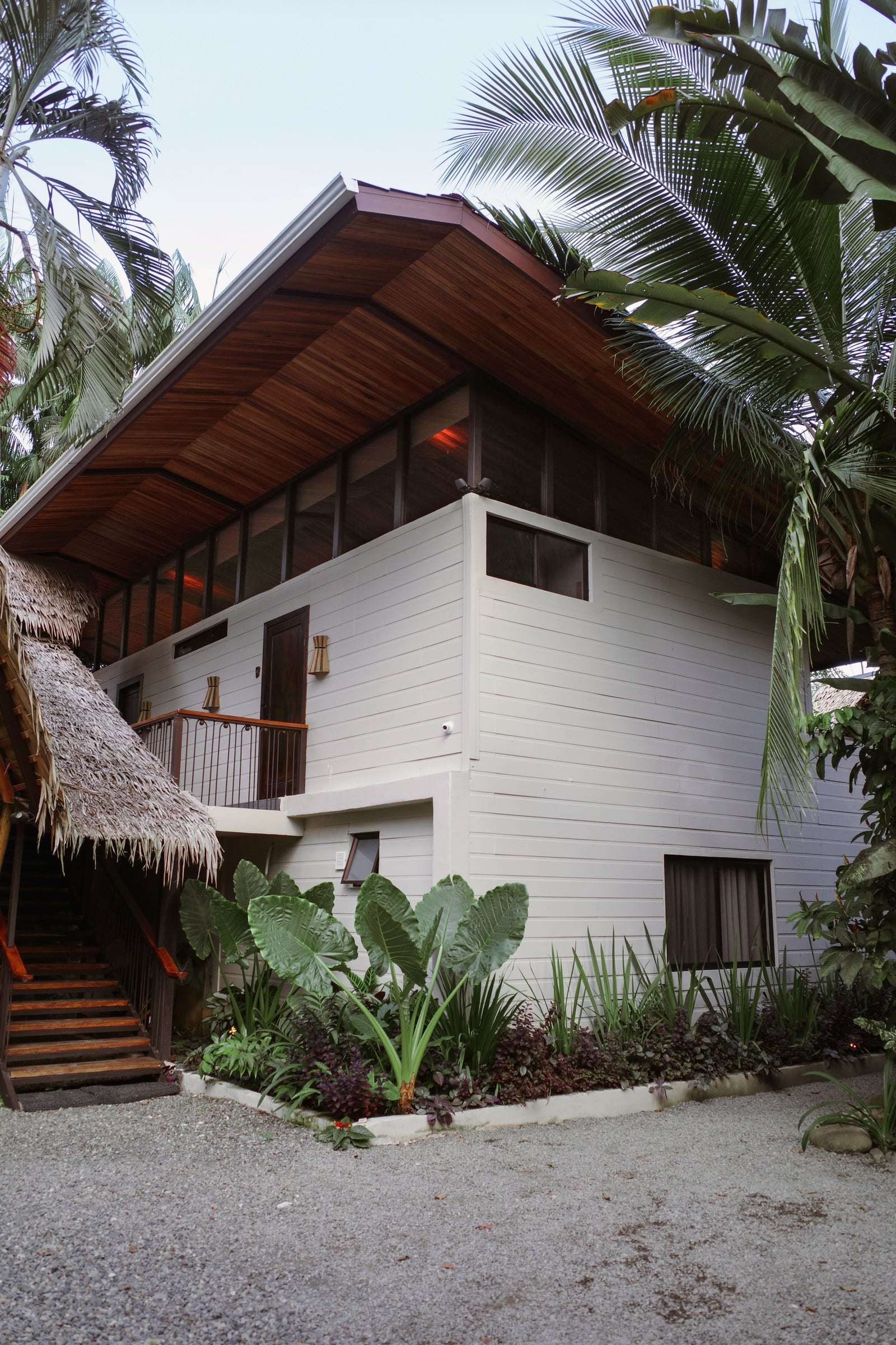 Two-storey wing of white clapboard with timber eaves and clerestory windows, beside the thatch and palms
