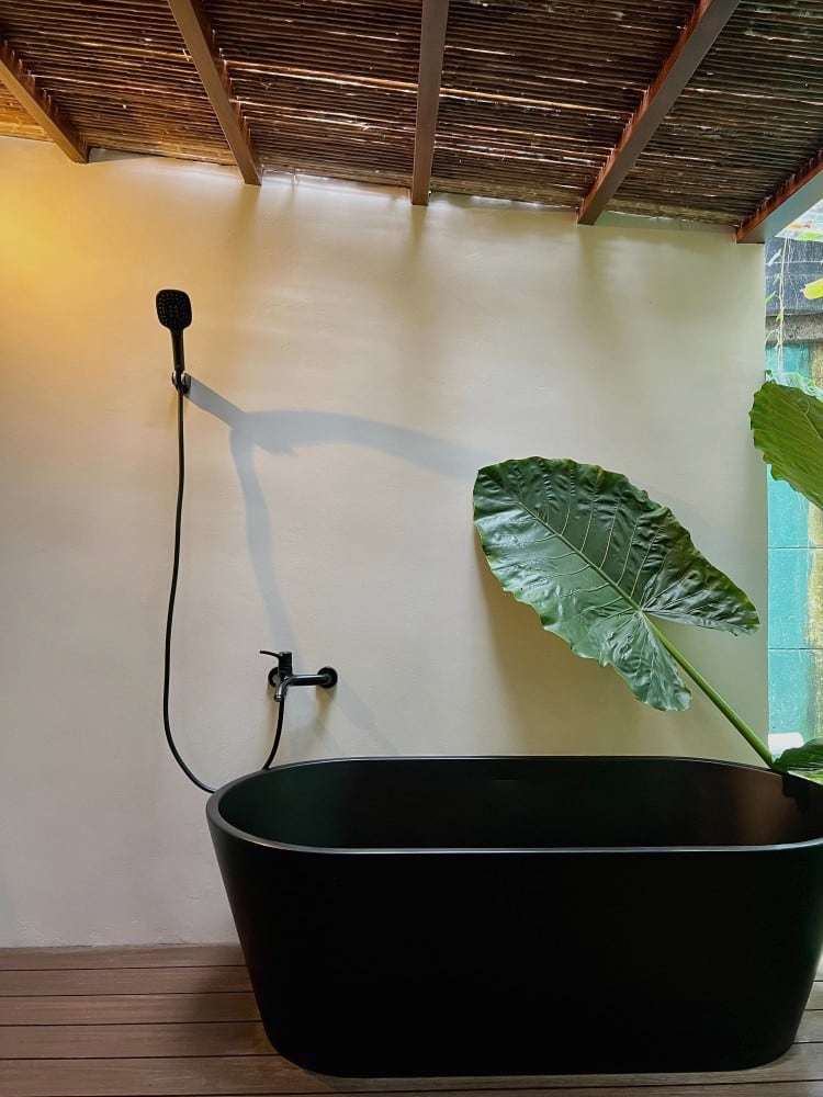 Grand Oasis Suite: black freestanding tub on the open-air deck, with hand shower, cane pergola and elephant-ear leaf