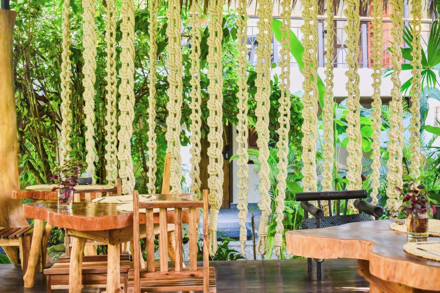 Rancho dining area: live-edge wooden tables and chairs before a curtain of hanging macramé ropes