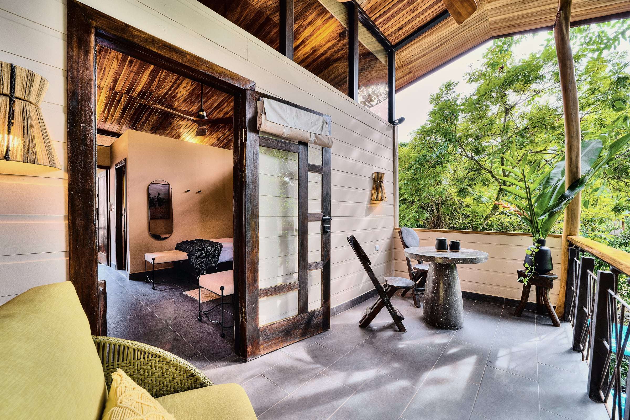 Jungle View Suite terrace: yellow armchair and terrazzo table among the treetops, glass door open to the bedroom