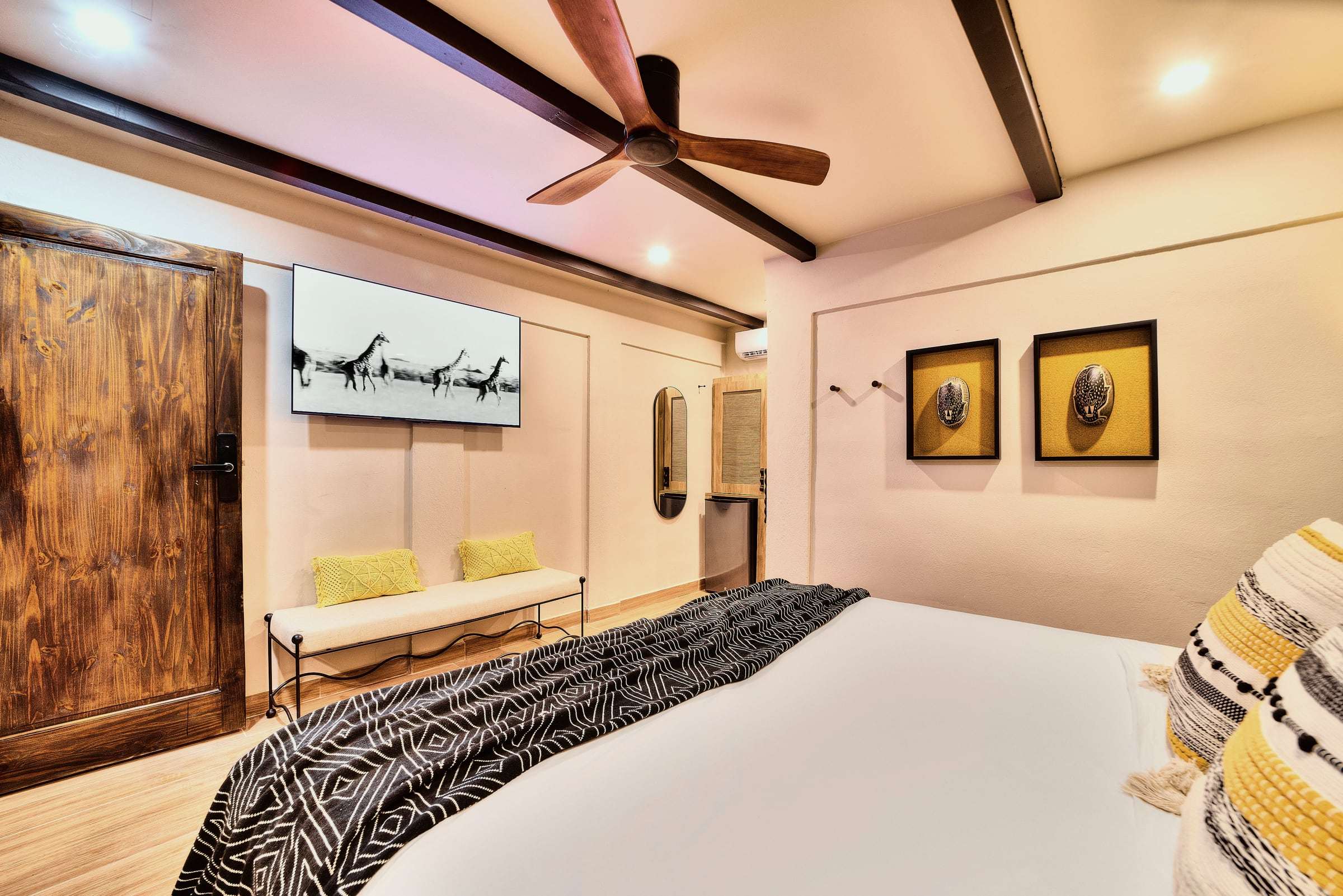 Deluxe Garden King: foot of the king bed facing a wall TV, cushioned bench, framed masks and a rustic wooden door
