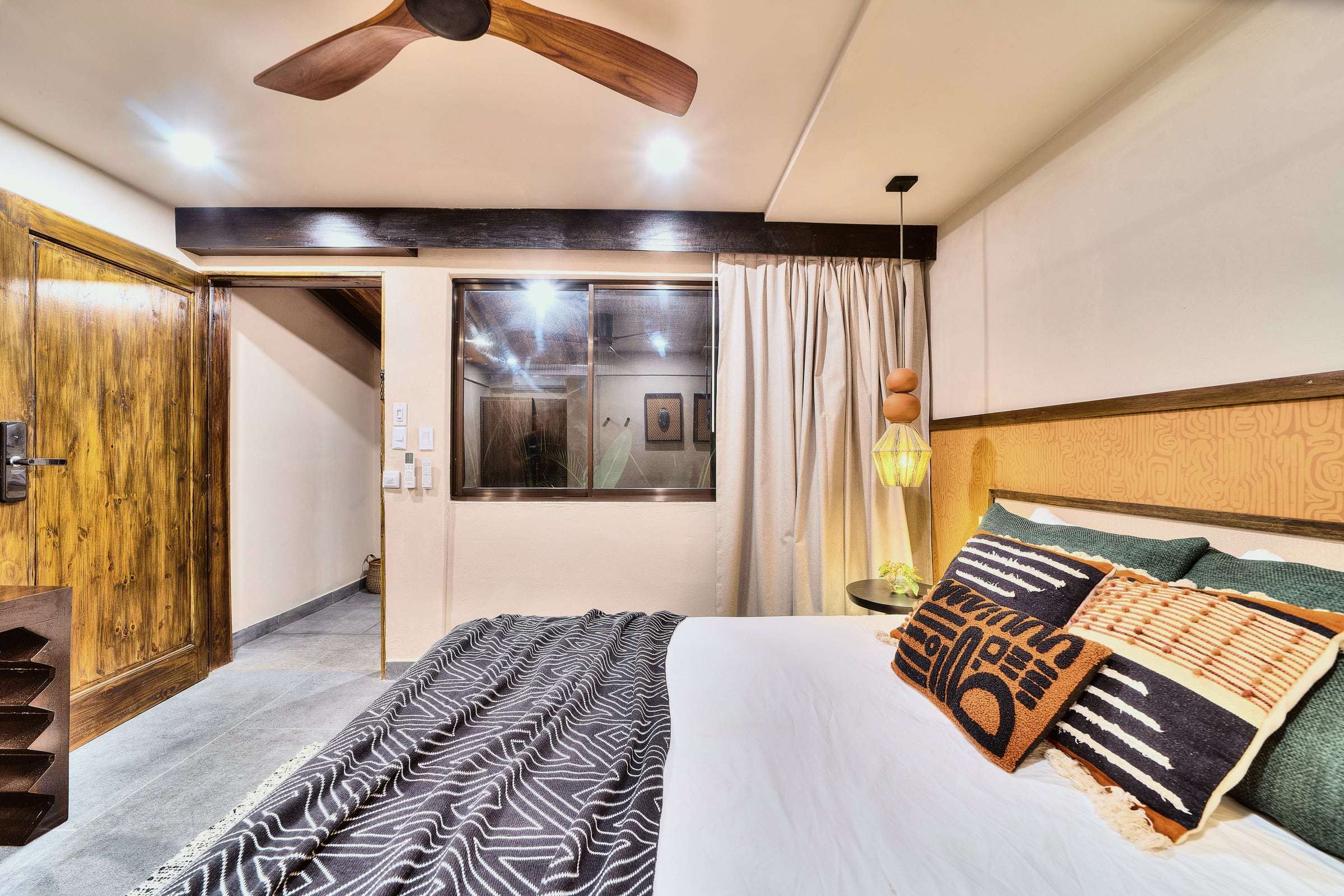 Deluxe Garden King: king bed with patterned cushions, ochre headboard wall, a beaded pendant lamp and wooden door