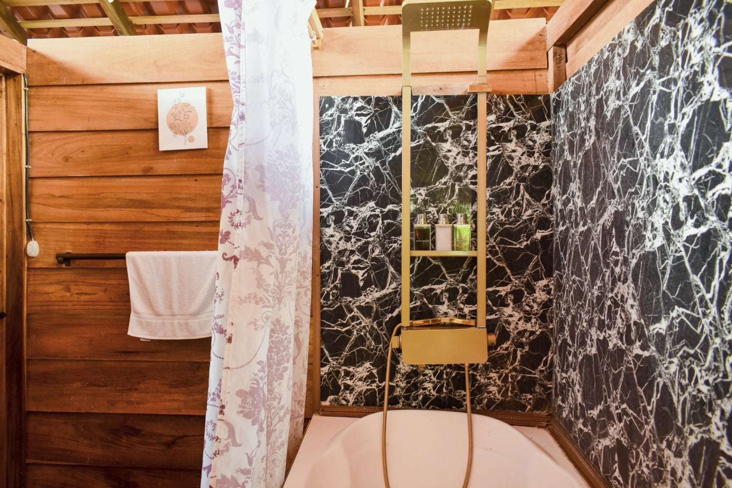Garden Home bathroom: bathtub with a brass-tone rain shower column, black marble-effect walls and wood panelling