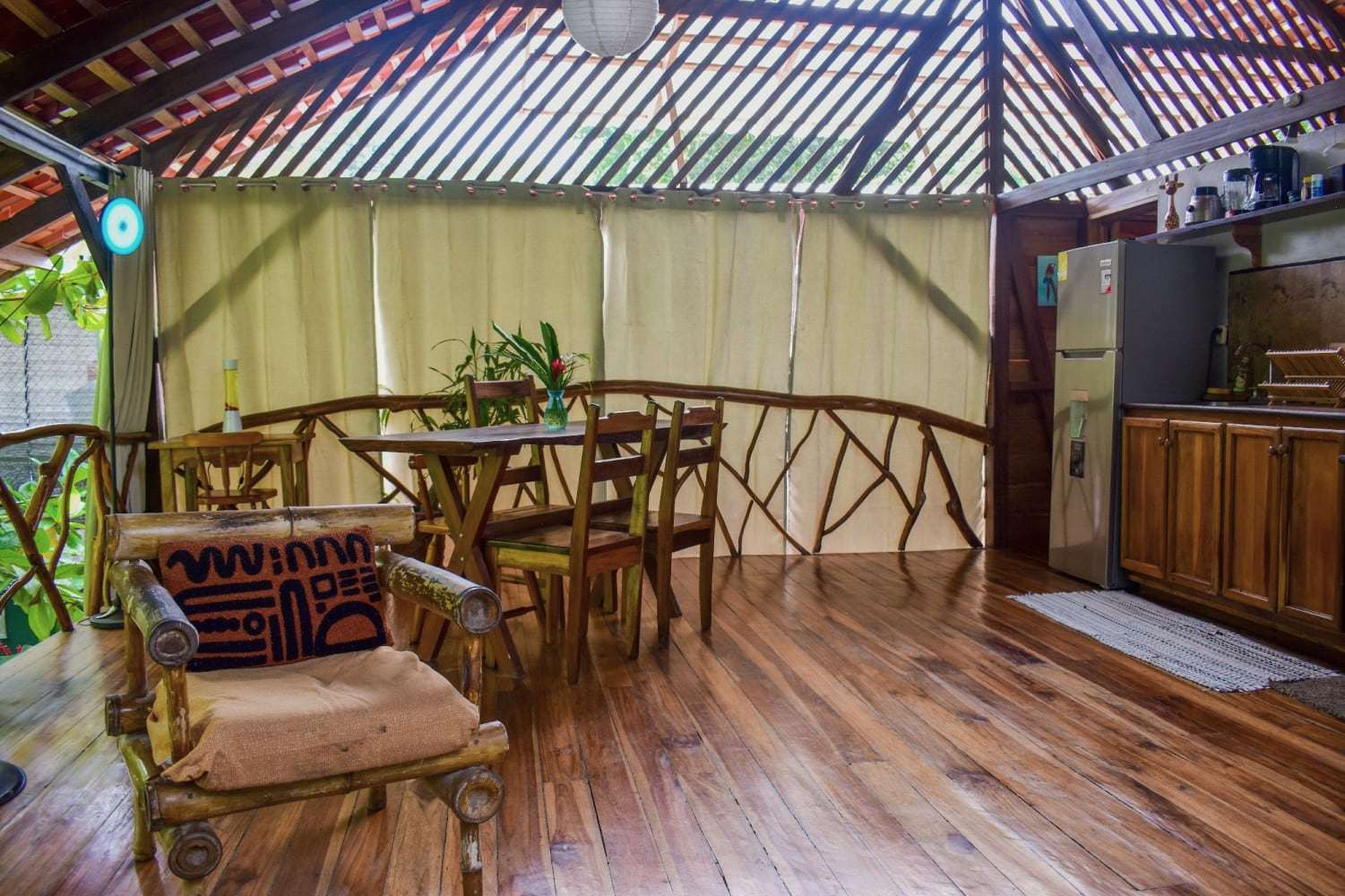 Garden Home dining table with wooden chairs and flowers, branch railings, and the kitchen to the right