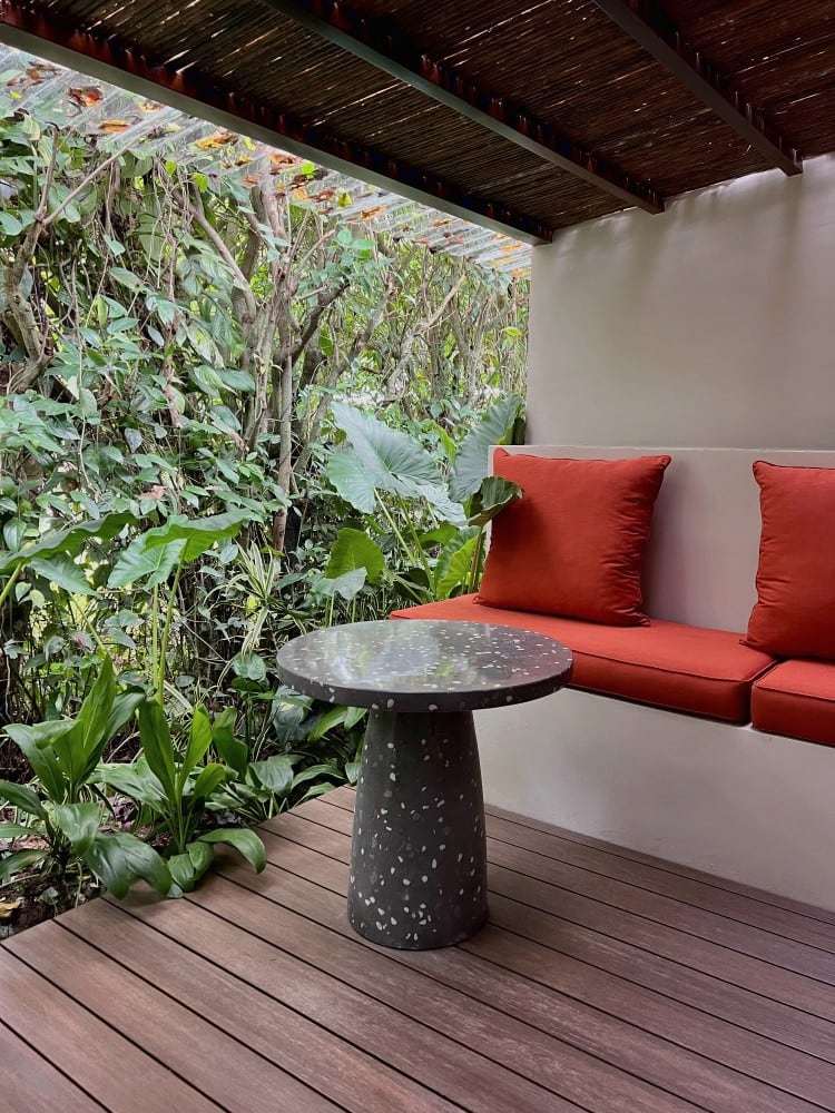 Grand Oasis Suite deck lounge: red-cushioned built-in bench and terrazzo table under a cane pergola, garden beyond