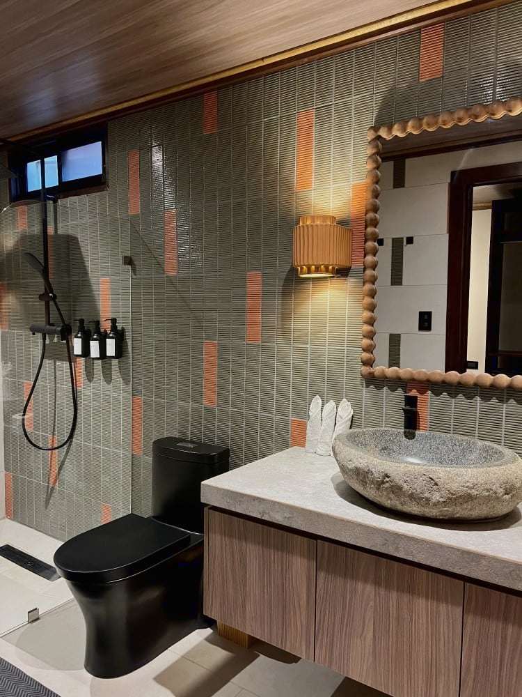 Grand Oasis Suite bathroom: sage and terracotta tiles, beaded wooden mirror, river-stone sink and rain shower