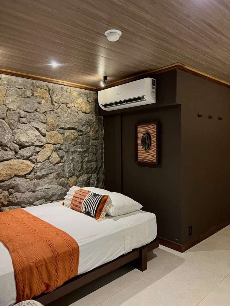 Grand Oasis Suite: bed with a burnt-orange throw against a hand-laid stone wall and a dark accent wall
