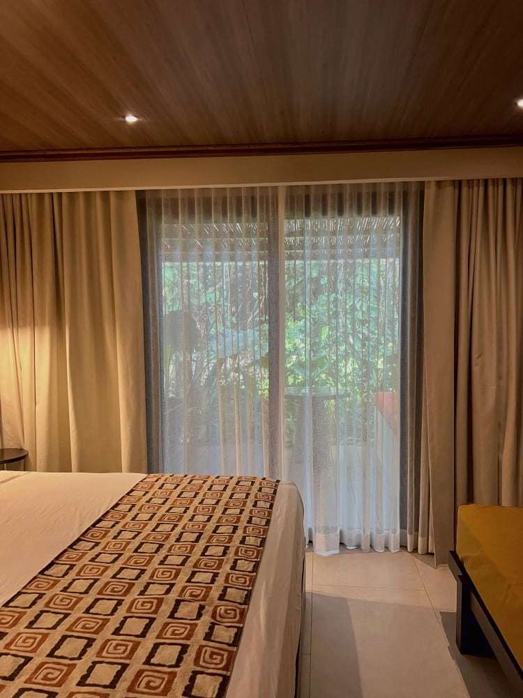 Grand Oasis Suite: foot of the bed with a geometric runner, facing sheer-curtained sliding doors to the garden