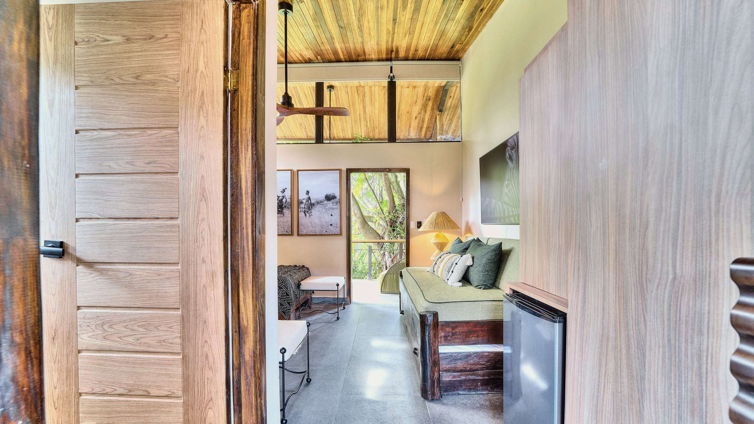Jungle View Suite from the entry door: green daybed, raffia lamp and bed, through to the terrace and treetops