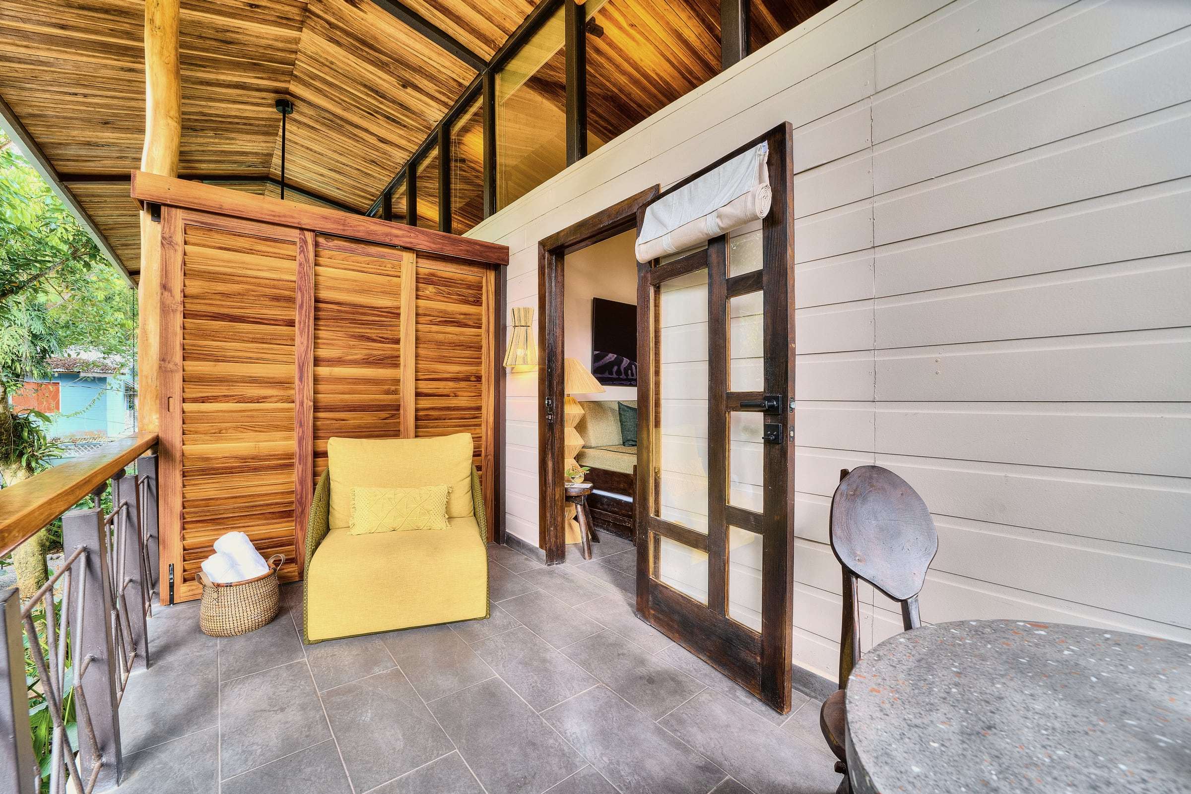 Jungle View Suite terrace: yellow armchair against wooden louvred screens, towel basket and a glass door to the room