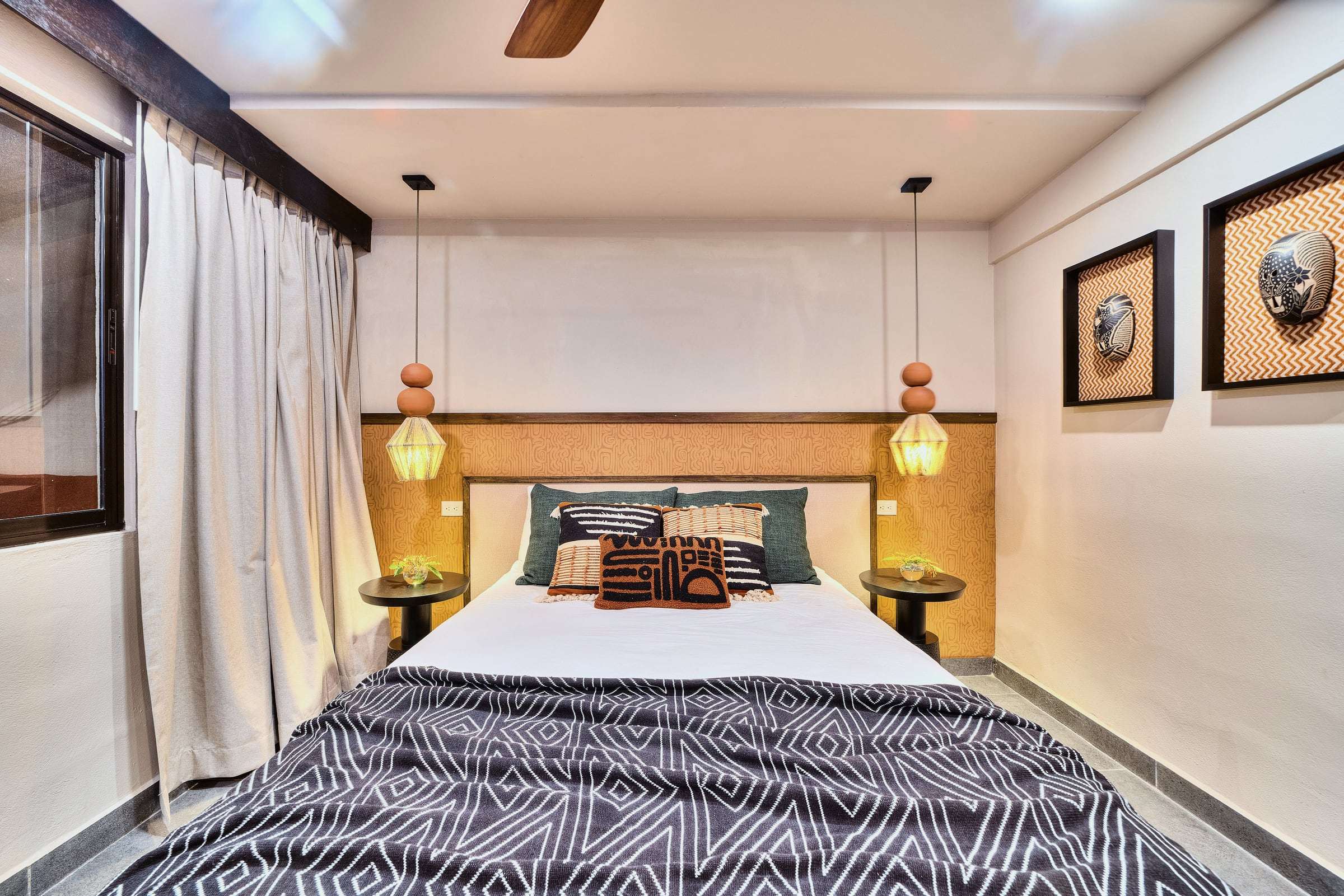 Superior Garden Room: queen bed with patterned cushions, ochre headboard wall, twin beaded pendants and framed masks