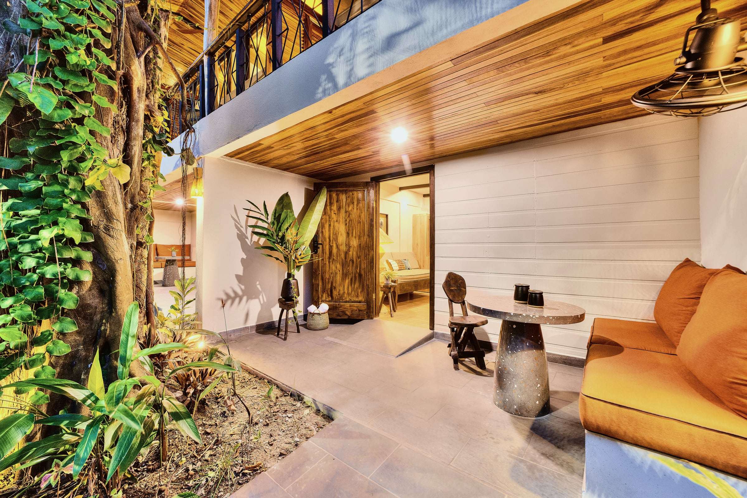 Superior Garden Room terrace: orange banquette, terrazzo table, carved chair and a vine-covered tree beside the door