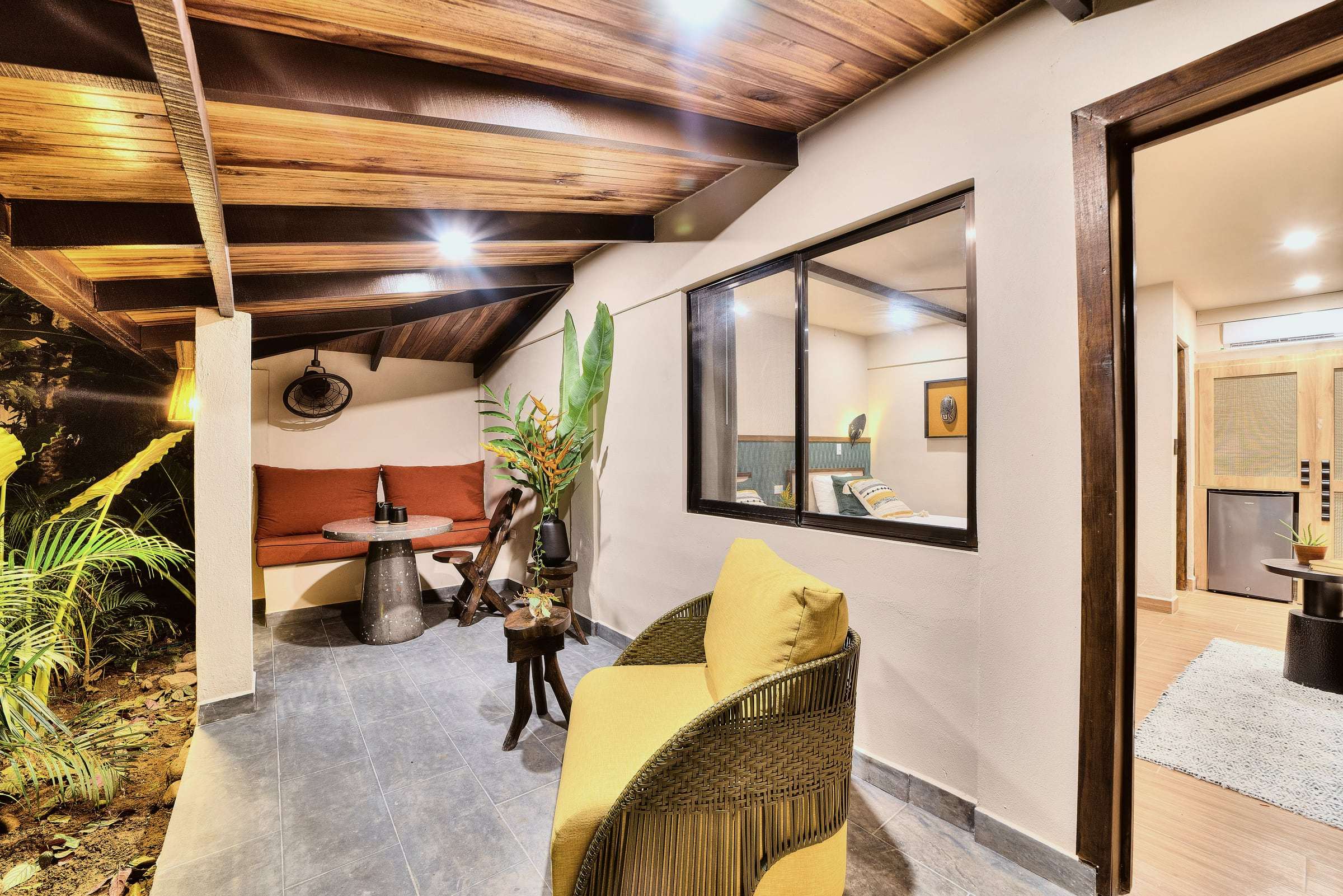 Superior Garden Room covered terrace with a yellow woven armchair, an orange banquette nook and a window into the room