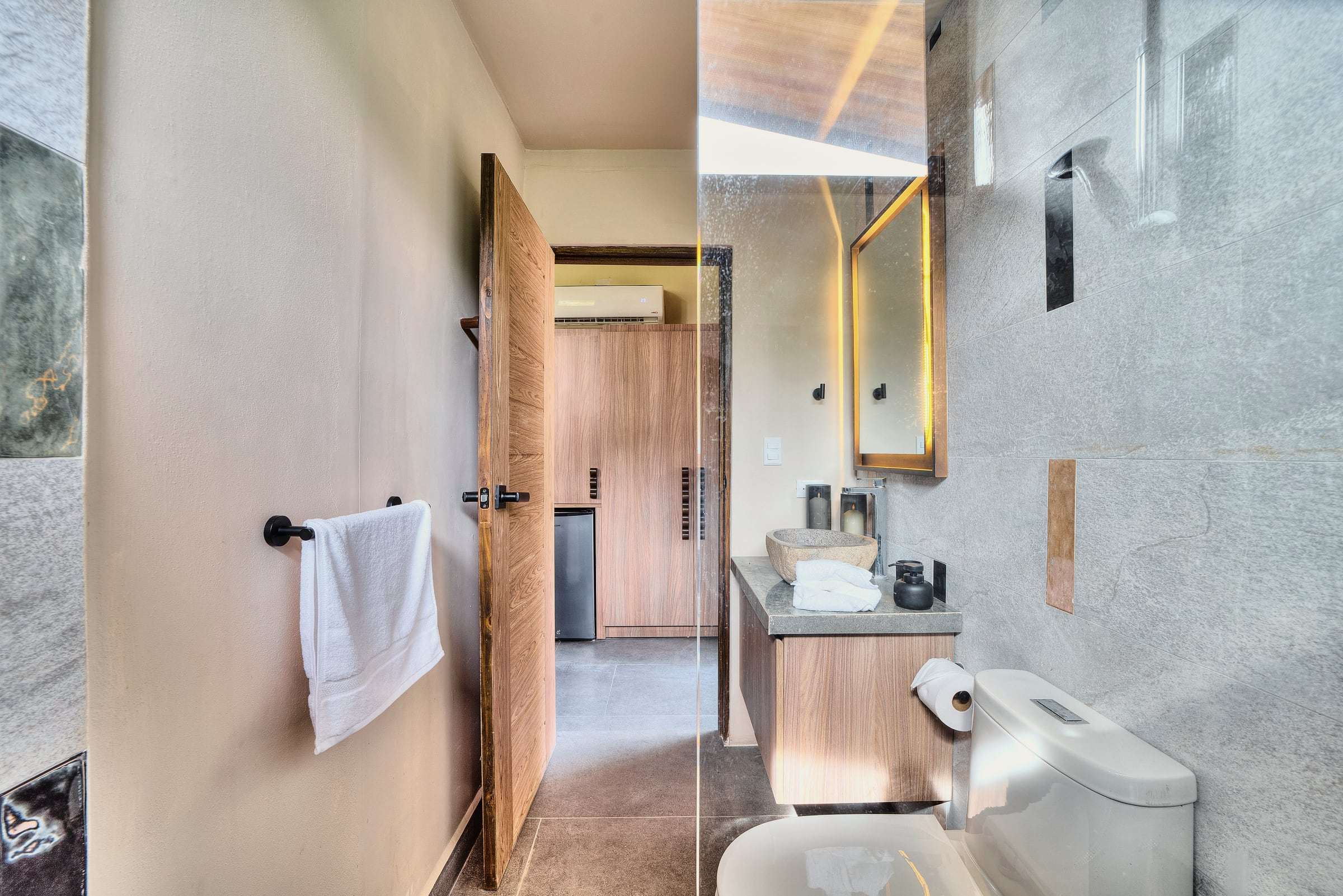 Terrace Suite bathroom seen from the shower: river-stone sink, backlit mirror and a door through to the bedroom